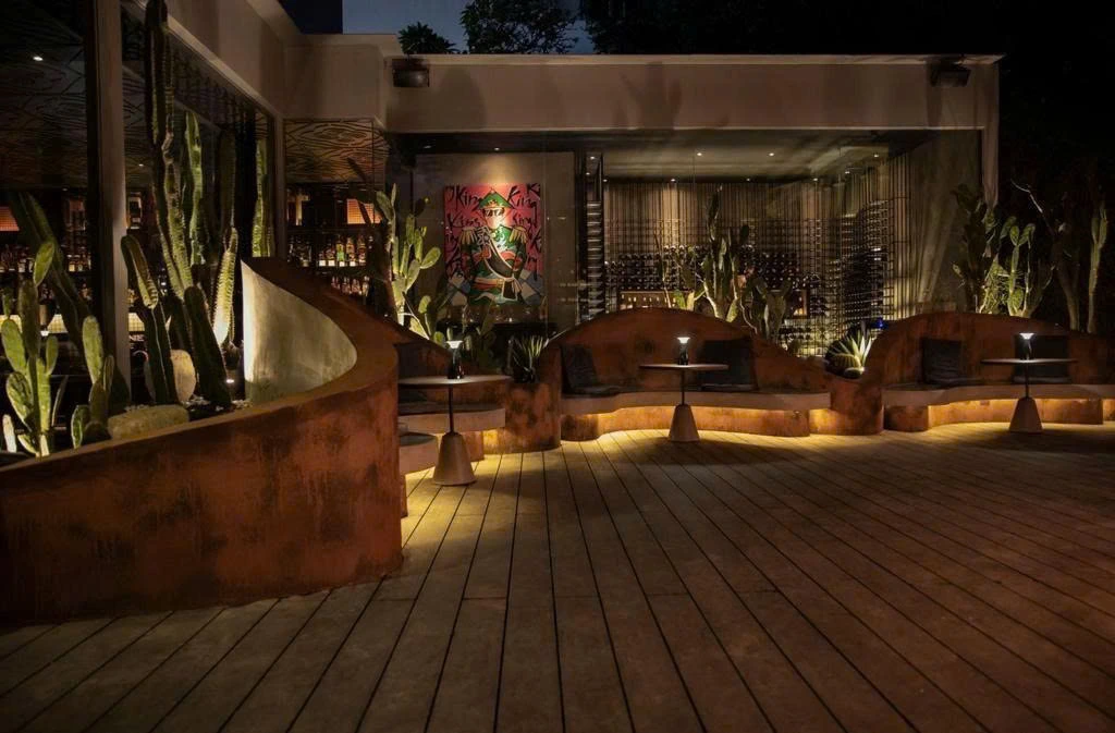 Warm rust-finish curved planter walls and built-in seating in the COCO project, with low evening lighting and dark timber decking.