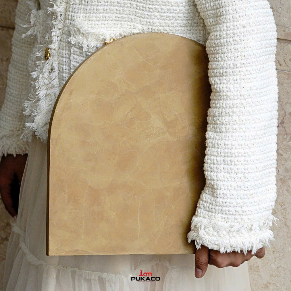 An ochre arched PUKACO sample rests against an ivory woven jacket.